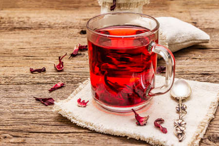 Hot hibiscus tea. Dry petals, linen sacks. Healthy food and self-care concept. Old wooden boards backgrounds, close upの写真素材