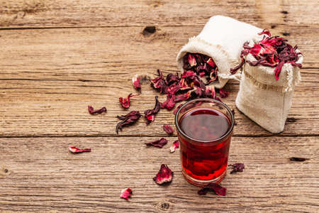 Hot hibiscus tea. Dry petals, linen sacks. Healthy food and self-care concept. Old wooden boards backgrounds, copy spaceの写真素材