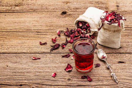 Hot hibiscus tea. Dry petals, linen sacks. Healthy food and self-care concept. Old wooden boards backgrounds, copy spaceの写真素材