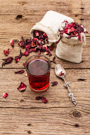 Hot hibiscus tea. Dry petals, linen sacks. Healthy food and self-care concept. Old wooden boards backgrounds, copy space, close upの写真素材