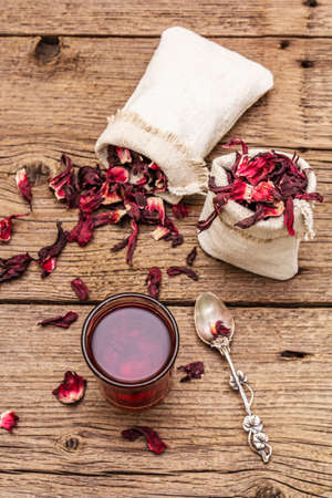 Hot hibiscus tea. Dry petals, linen sacks. Healthy food and self-care concept. Old wooden boards backgrounds, top view, close upの写真素材