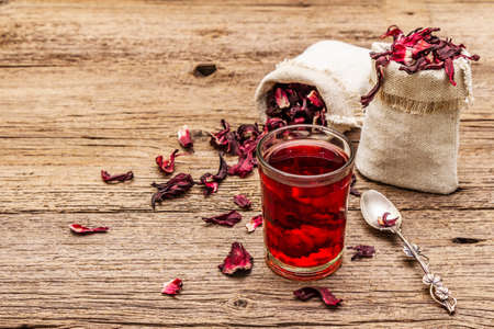 Hot hibiscus tea. Dry petals, linen sacks. Healthy food and self-care concept. Old wooden boards backgrounds, copy space, close upの写真素材
