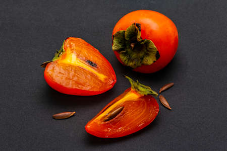 Ripe single persimmon. Fresh whole fruit, half sliced, seeds. Isolated on matte black background, close upの写真素材