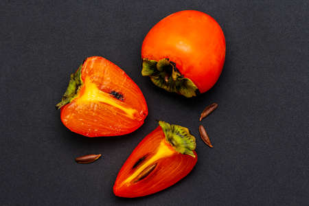 Ripe single persimmon. Fresh whole fruit, half sliced, seeds. Isolated on matte black background, top viewの写真素材