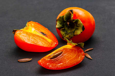 Ripe single persimmon. Fresh whole fruit, half sliced, seeds. Isolated on matte black background, close upの写真素材