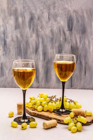 Wine glasses, fresh grapes and corks on wooden chopping board. Wine bar, winery, wine tasting concept. Stone concrete background, copy spaceの写真素材