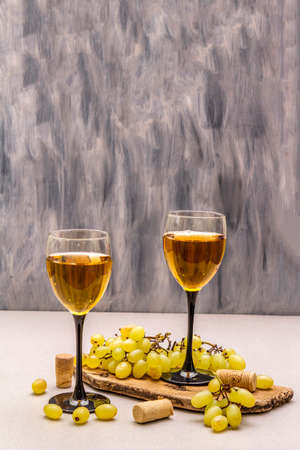 Wine glasses, fresh grapes and corks on wooden chopping board. Wine bar, winery, wine tasting concept. Stone concrete background, copy spaceの写真素材