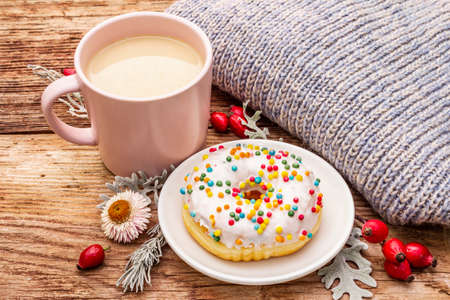 Hot coffee with a donut. Autumn drink for a good mood with plaid, fresh rose hips, leaves and flowers. Old wood plank background, close upの写真素材