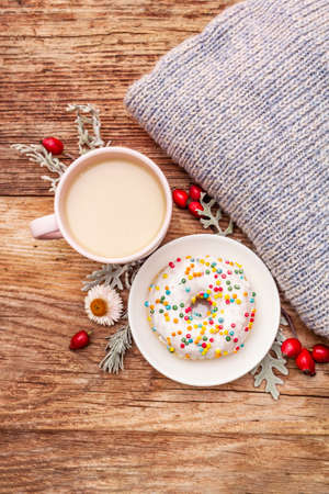 Hot coffee with a donut. Autumn drink for a good mood with plaid, fresh rose hips, leaves and flowers. Old wood plank background, copy space, top viewの写真素材