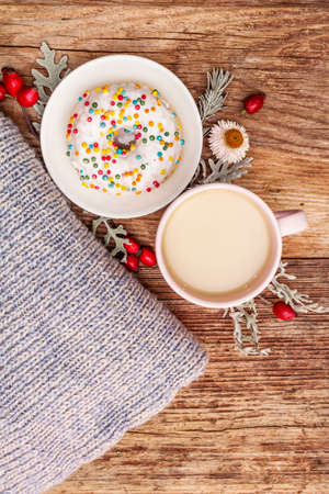 Hot coffee with a donut. Autumn drink for a good mood with plaid, fresh rose hips, leaves and flowers. Old wood plank background, copy space, top viewの写真素材
