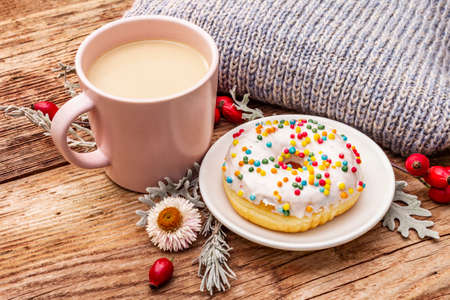 Hot coffee with a donut. Autumn drink for a good mood with plaid, fresh rose hips, leaves and flowers. Old wood plank background, close upの写真素材