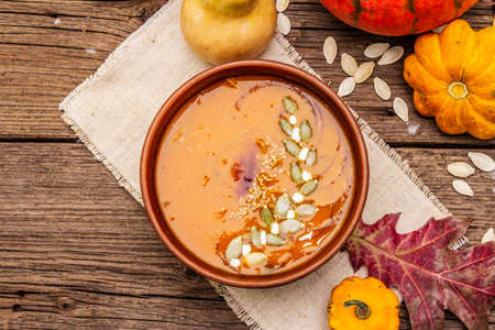 Autumn pumpkin cream soup. Traditional ingredients, healthy food concept. Napkin, vintage wooden background, copy space, top viewの写真素材