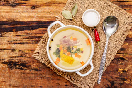 Transparent duck broth in bowl with vegetables. Traditional bouillon, healthy meal. Old wooden background, copy space, top viewの写真素材