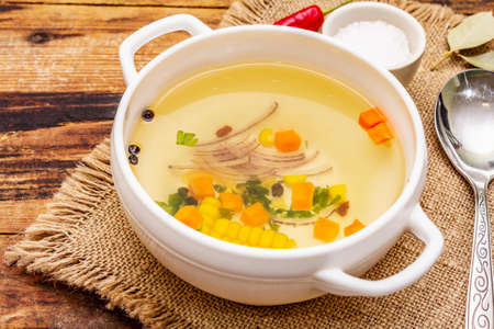 Transparent duck broth in bowl with vegetables. Traditional bouillon, healthy meal. Old wooden background, close upの写真素材