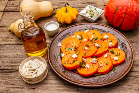 Roasted pumpkin with salted cheese and herbs. Healthy vegetarian snack. Oil, Feta, sesame seeds. Wooden boards background, copy spaceの写真素材