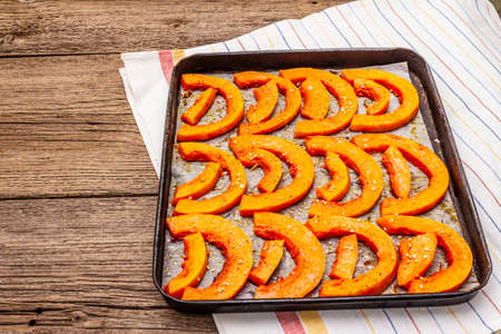 Baked pumpkin with vegetable oil, sesame seeds and spices. Vegan (vegetarian) healthy food concept. Metal pan on a wooden background, copy spaceの写真素材