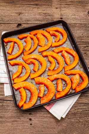 Baked pumpkin with vegetable oil, sesame seeds and spices. Vegan (vegetarian) healthy food concept. Metal pan on a wooden background, copy space, close upの写真素材