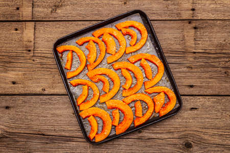 Baked pumpkin with vegetable oil, sesame seeds and spices. Vegan (vegetarian) healthy food concept. Metal pan on a wooden background, top view, copy spaceの写真素材