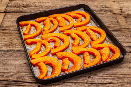 Baked pumpkin with vegetable oil, sesame seeds and spices. Vegan (vegetarian) healthy food concept. Metal pan on a wooden background, close upの写真素材