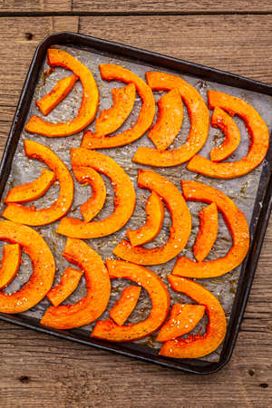 Baked pumpkin with vegetable oil, sesame seeds and spices. Vegan (vegetarian) healthy food concept. Metal pan on a wooden background, close upの写真素材