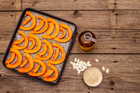Baked pumpkin with vegetable oil, sesame seeds and spices. Vegan (vegetarian) healthy food concept. Metal pan on a wooden background, copy space, top viewの写真素材