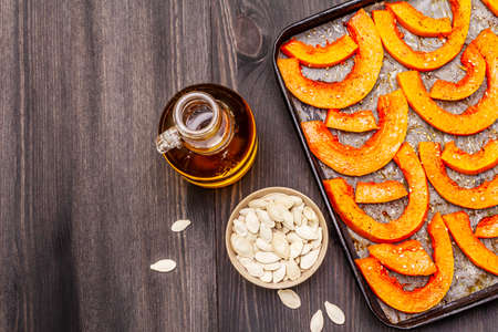 Baked pumpkin with vegetable oil, sesame seeds and spices. Vegan (vegetarian) healthy food concept. Metal pan on a black wooden background, copy spaceの写真素材