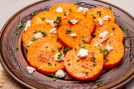 Roasted pumpkin with salted cheese and herbs. Healthy vegetarian snack. Vintage napkins, stone concrete background, close upの写真素材