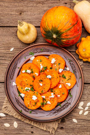 Roasted pumpkin with salted cheese and herbs. Healthy vegetarian snack. Vintage napkin, wooden boards background, top view, close upの写真素材
