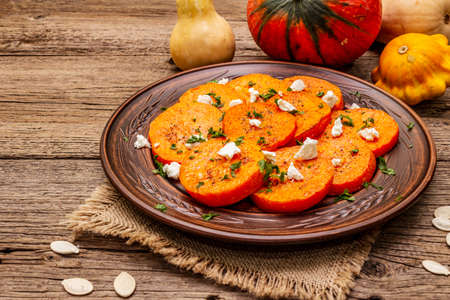 Roasted pumpkin with salted cheese and herbs. Healthy vegetarian snack. Vintage napkin, wooden boards background, close upの写真素材