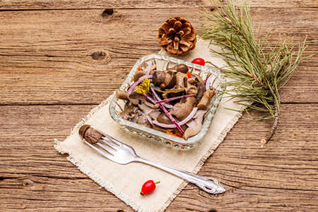 Pickled or fermented mushrooms. Traditional Christmas snack. New Year Festive cutlery. Evergreen pine, cone, spices, crystal plate. Wooden boards background, copy spaceの写真素材