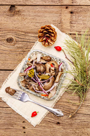 Pickled or fermented mushrooms. Traditional Christmas snack. New Year Festive cutlery. Evergreen pine, cone, spices, crystal plate. Wooden boards background, copy space, top viewの写真素材