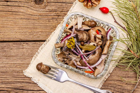 Pickled or fermented mushrooms. Traditional Christmas snack. New Year Festive cutlery. Evergreen pine, cone, spices, crystal plate. Wooden boards background, copy space, top viewの写真素材