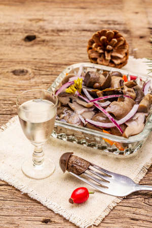 Pickled or fermented mushrooms. Traditional Christmas snack. New Year Festive cutlery. Evergreen pine, cone, spices, glass of vodka. Wooden boards background, close upの写真素材