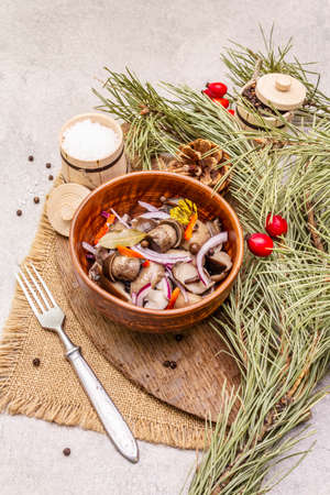 Pickled or fermented mushrooms. Traditional Christmas snack. New Year Festive cutlery. Evergreen pine, cone, spices, chopping board. Stone concrete background, close upの写真素材