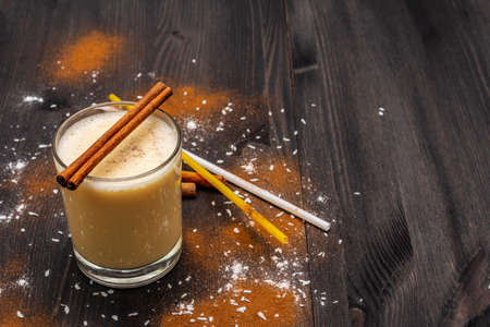 Traditional winter eggnog with milk, rum and cinnamon, sprinkle with grated nutmeg. Cocktail straws, dark wooden background, copy spaceの写真素材
