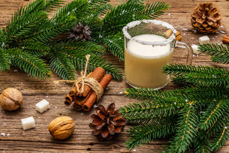 Christmas eggnog liqueur or cola de mono cocktail. Classical winter drink in glass mug, xmas decorations. Evergreen branches, cinnamon, walnuts, sugar. Old wooden background, close upの写真素材