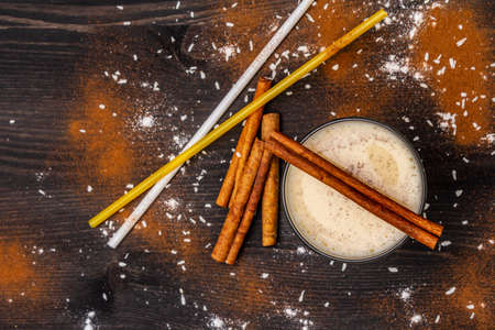 Traditional winter eggnog with milk, rum and cinnamon, sprinkle with grated nutmeg. Cocktail straws, dark wooden background, top view, close upの写真素材