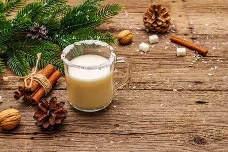 Christmas eggnog liqueur or cola de mono cocktail. Classical winter drink in glass mug, xmas decorations. Evergreen branches, cinnamon, walnuts, sugar. Old wooden background, copy spaceの写真素材