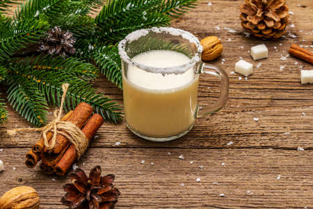 Christmas eggnog liqueur or cola de mono cocktail. Classical winter drink in glass mug, xmas decorations. Evergreen branches, cinnamon, walnuts, sugar. Old wooden background, copy spaceの写真素材