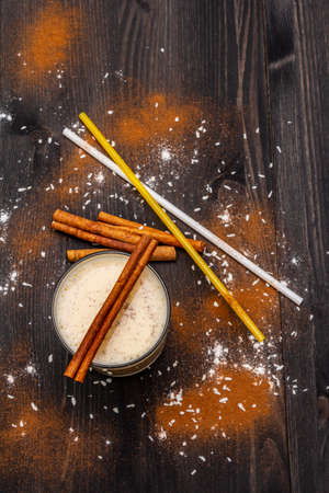 Traditional winter eggnog with milk, rum and cinnamon, sprinkle with grated nutmeg. Cocktail straws, dark wooden background, top view, close upの写真素材