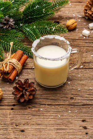 Christmas eggnog liqueur or cola de mono cocktail. Classical winter drink in glass mug, xmas decorations. Evergreen branches, cinnamon, walnuts, sugar. Old wooden background, copy space, close upの写真素材