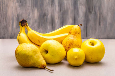 Assorted bright yellow fruits. Fresh banana, pear, apple, lemon. Harvest on a stone background, close upの写真素材