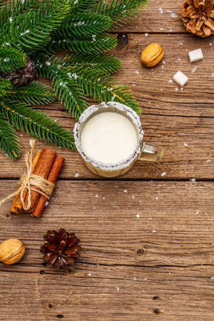 Christmas eggnog liqueur or cola de mono cocktail. Classical winter drink in glass mug, xmas decorations. Evergreen branches, cinnamon, walnuts, sugar. Old wooden background, copy space, top viewの写真素材