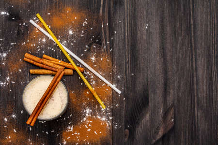 Traditional winter eggnog with milk, rum and cinnamon, sprinkle with grated nutmeg. Cocktail straws, dark wooden background, copy space, top viewの写真素材