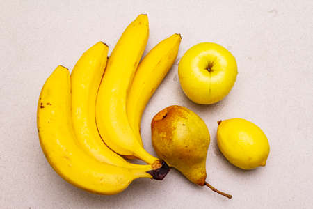 Assorted bright yellow fruits. Fresh banana, pear, apple, lemon. Harvest on a stone background, top view, close upの写真素材