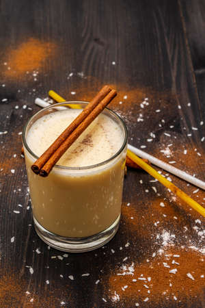 Traditional winter eggnog with milk, rum and cinnamon, sprinkle with grated nutmeg. Cocktail straws, dark wooden background, close upの写真素材