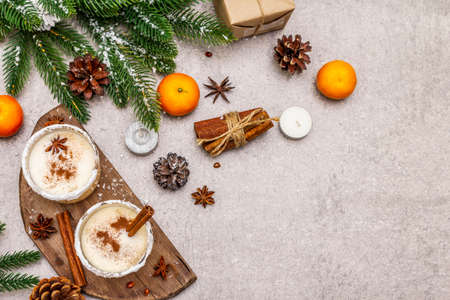 Eggnog with cinnamon and nutmeg for Christmas and winter holidays. Homemade beverage in glasses with spicy rim. Tangerines, candles, gift. Stone concrete background, copy space, top viewの写真素材