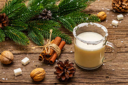 Christmas eggnog liqueur or cola de mono cocktail. Classical winter drink in glass mug, xmas decorations. Evergreen branches, cinnamon, walnuts, sugar. Old wooden background, close upの写真素材