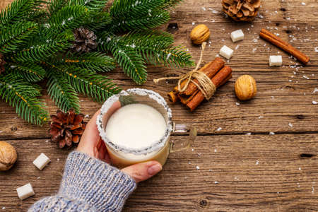 Christmas eggnog liqueur or cola de mono cocktail. Classical winter drink in glass mug, xmas decorations. Woman's hand in jersey. Old wooden background, copy spaceの写真素材