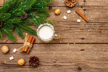 Christmas eggnog liqueur or cola de mono cocktail. Classical winter drink in glass mug, xmas decorations. Evergreen branches, cinnamon, walnuts, sugar. Old wooden background, copy space, top viewの写真素材